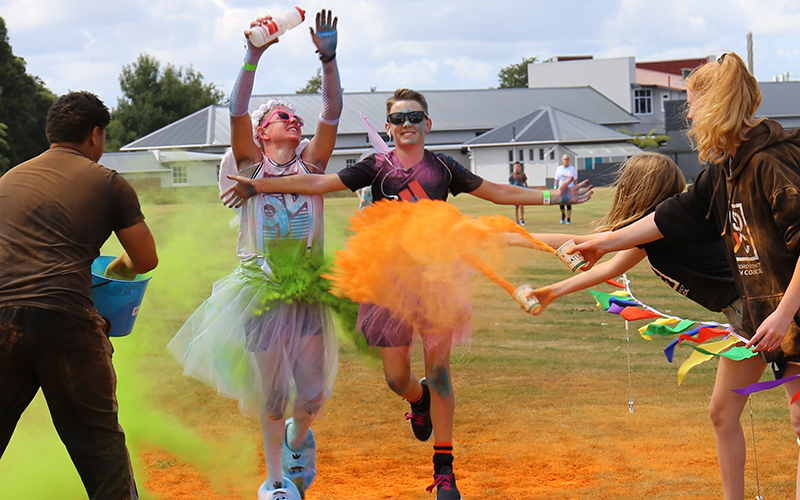 People throw coloured powder on two teenage runners dressed in costume.