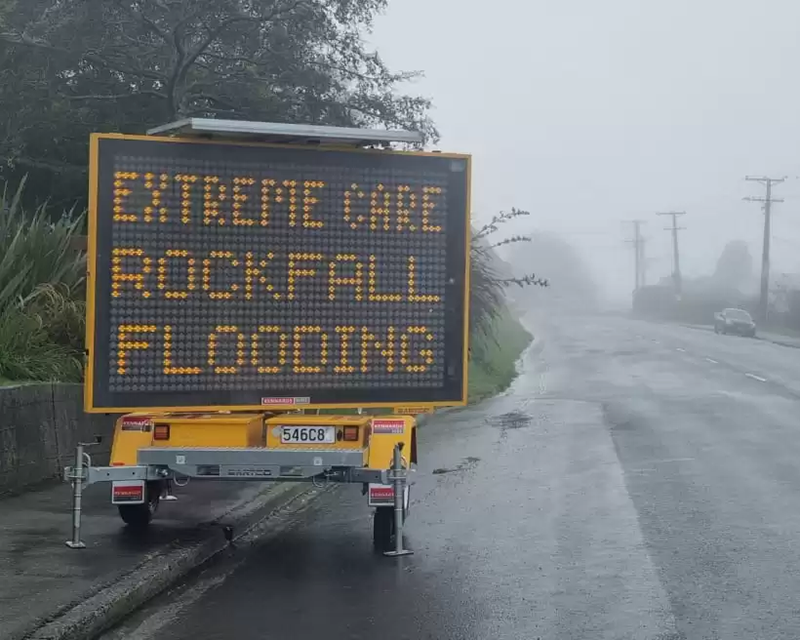 Electronic road sign outside in rainy weather. Text on side reads  "Extreme care rockfall flooding"