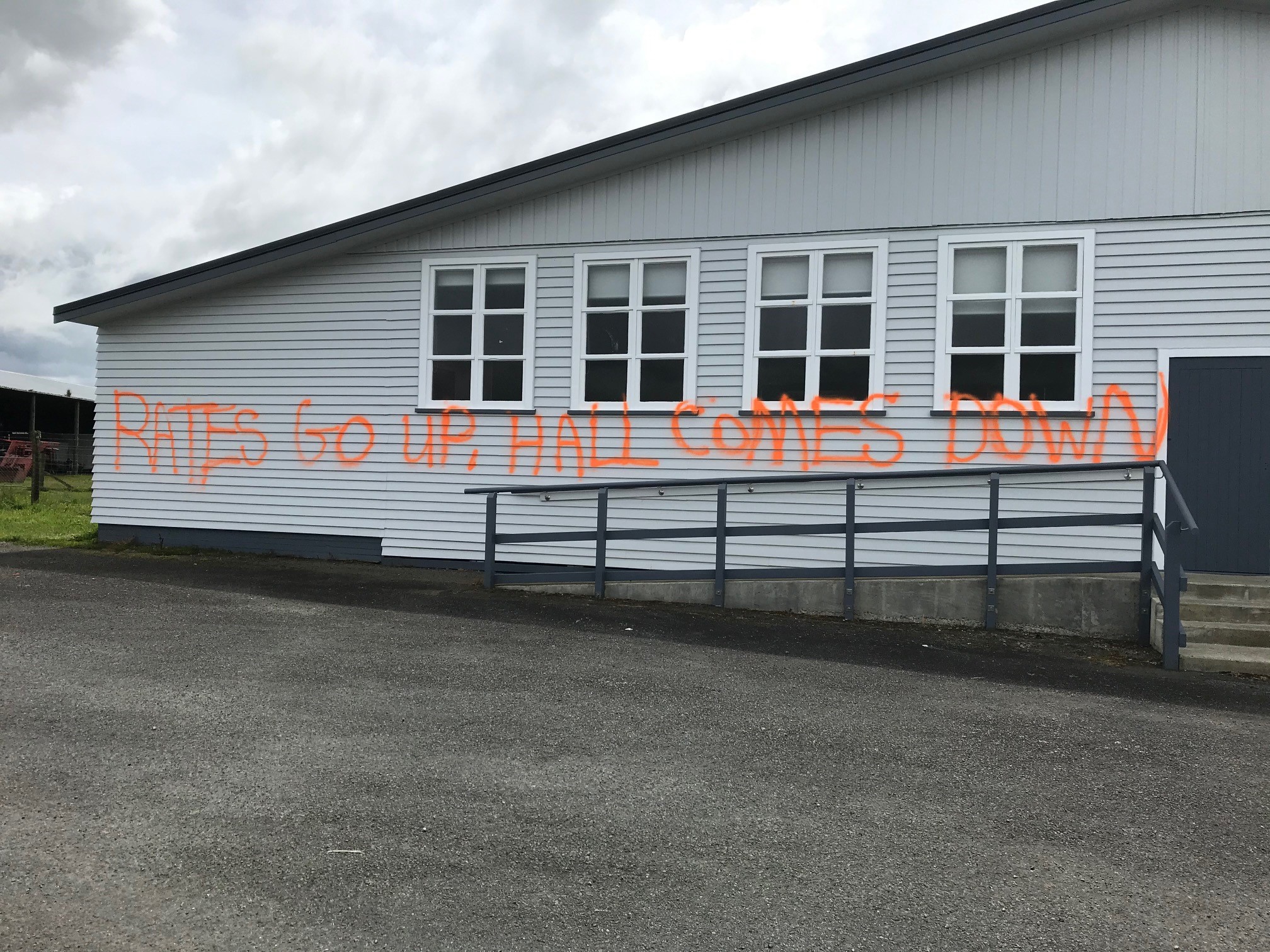 Photo of Midhirst Hall with graffiti writing that says 'Rates go up, hall comes down'